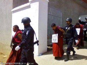 monks with placards around their necks are lead away from their monastery